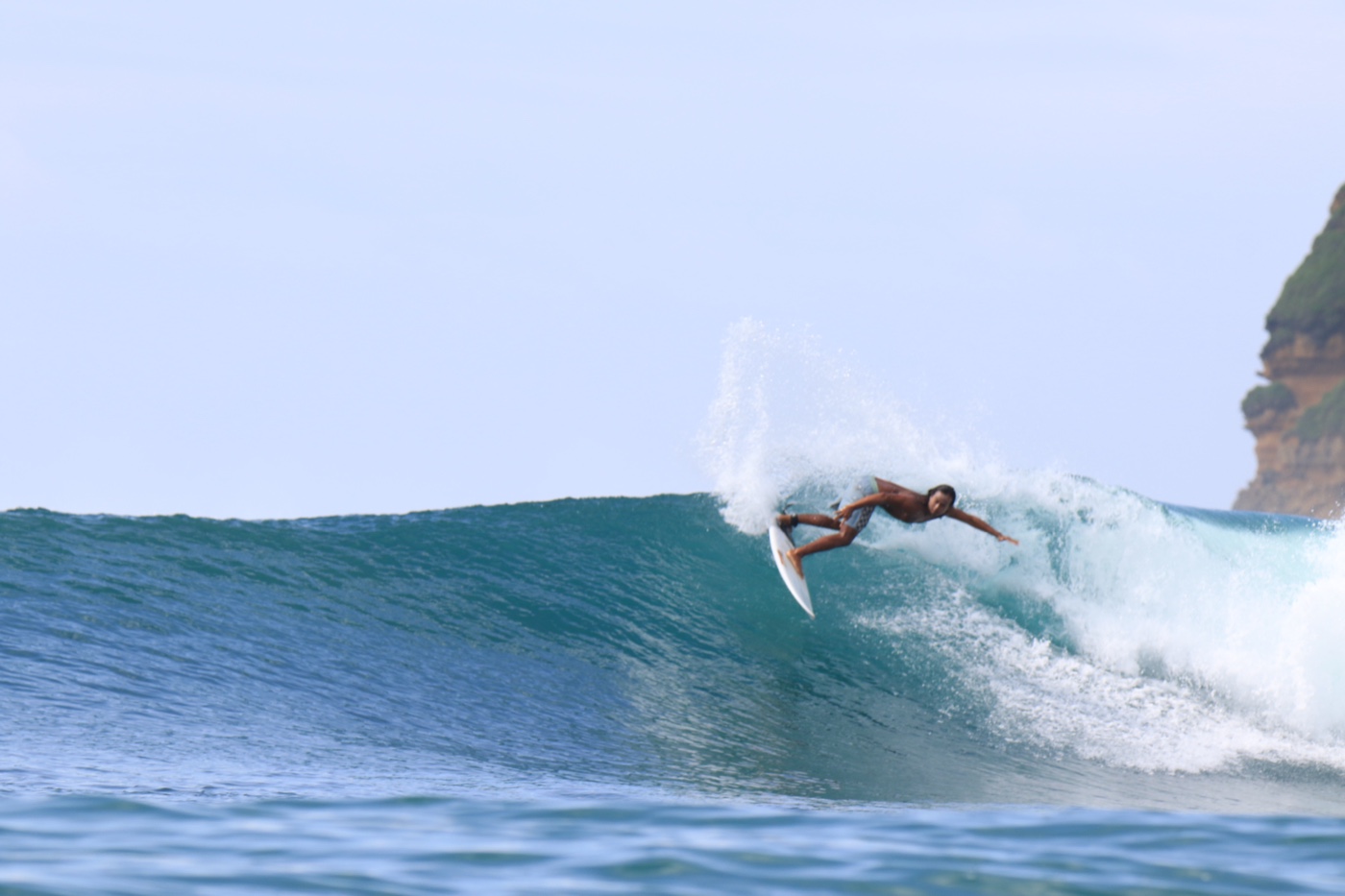 A surfer hitting the top of a breaking wave, spray fanning out behind the board.