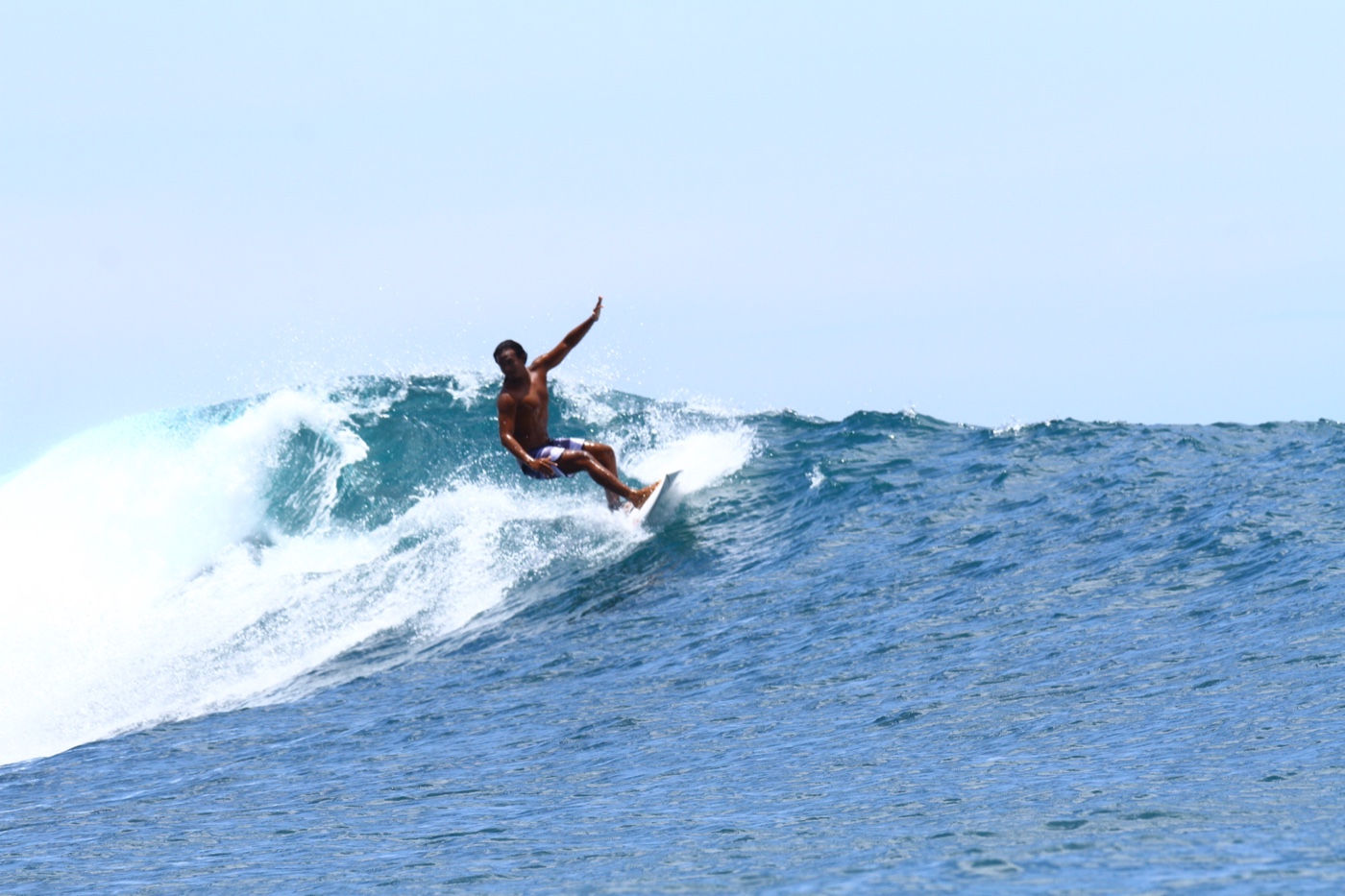 A surfer standing tall with one arm extended, riding along the open face of a wave.