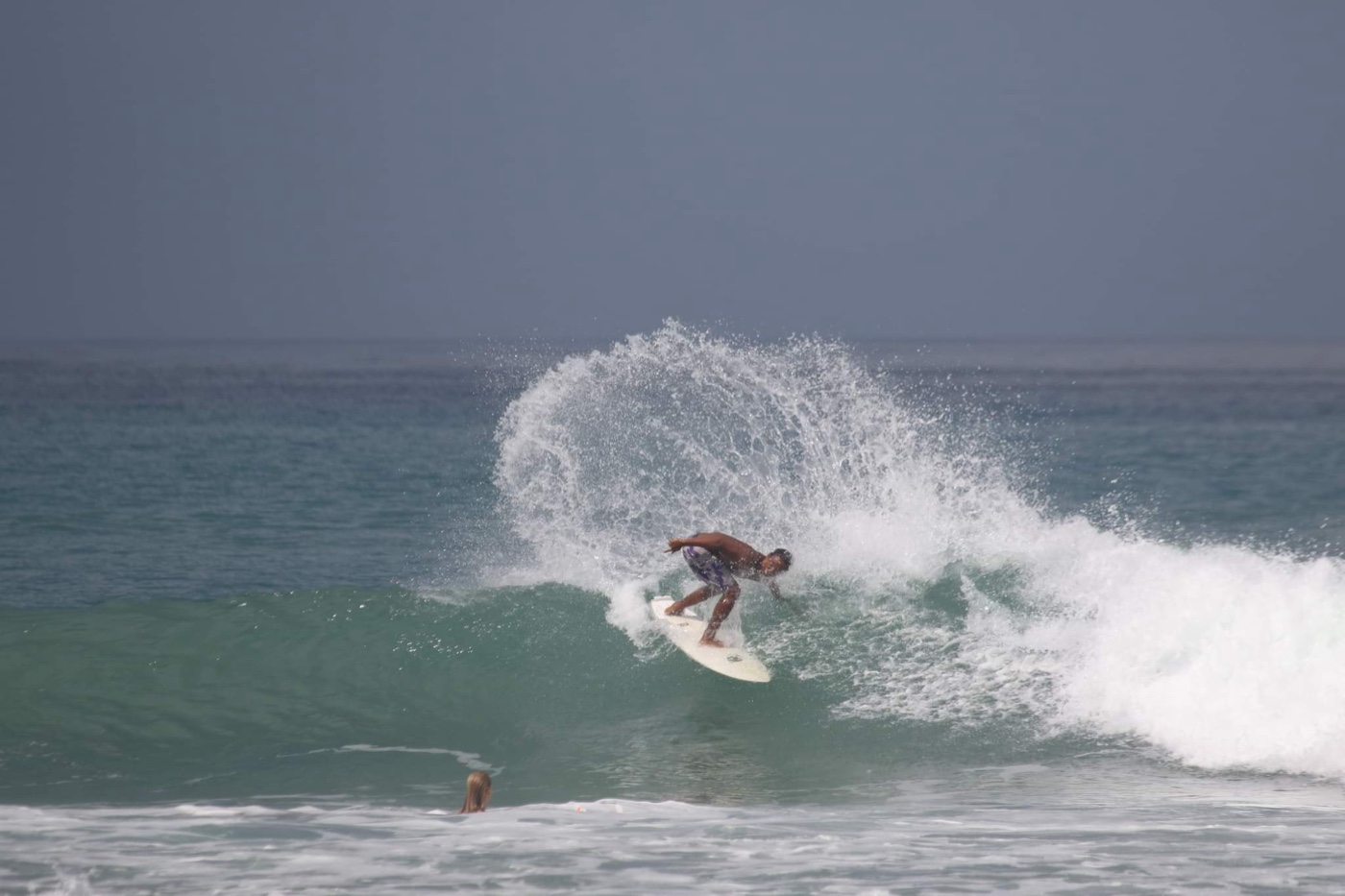 A surfer carving a sharp turn on a green wave, a fan of spray thrown out behind the board.